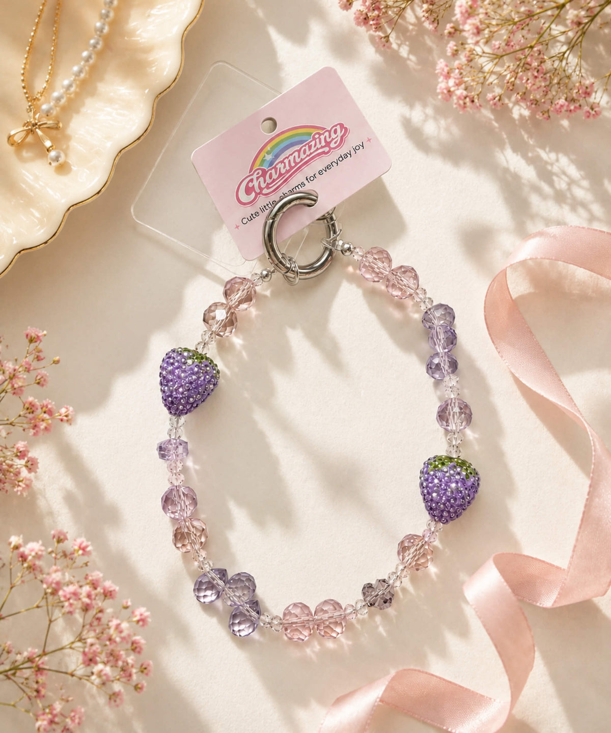 Strawberry beaded phone charm with pastel pink and lilac crystal-style beads in a soft floral lifestyle setting