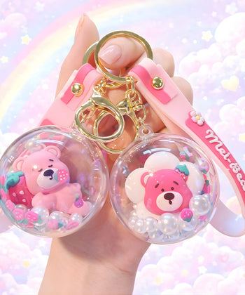 Strawberry bear bead shaker keychain set held in hand with pastel rainbow cloud background, cute kawaii floating pearl charm