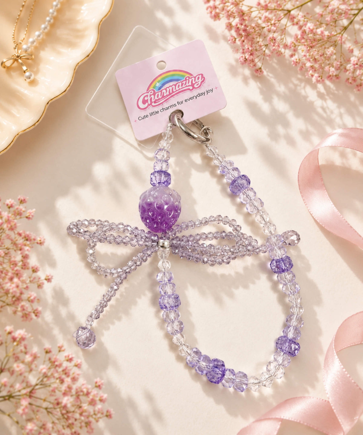 Purple strawberry bow beaded phone charm styled in a soft pastel lifestyle setting